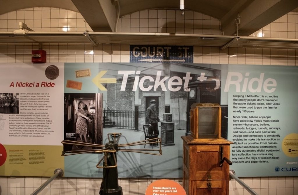 24 hours in NYC: Exhibit at the New York Transit Museum displaying the history of subway fares with vintage turnstiles, tokens, and large informational posters with text detailing the evolution from 'A Nickel a Ride' to modern MetroCard swipes.